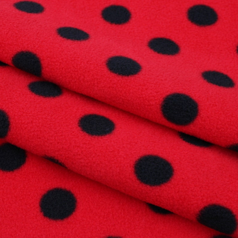 May include: Red fleece fabric with a black polka dot pattern. The fabric is folded in thirds, showing the pattern on each layer.