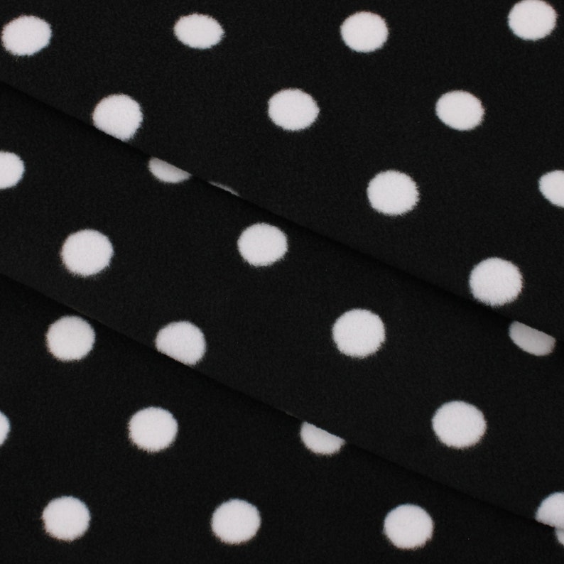 May include: Black fleece fabric with white polka dots. The fabric is folded in thirds, showing the pattern.