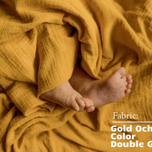 Pu&ograve; includere: I piedi di un bambino sono avvolti in un morbido tessuto di garza doppia giallo. Il tessuto &egrave; descritto come "Doppia garza color ocra dorata".