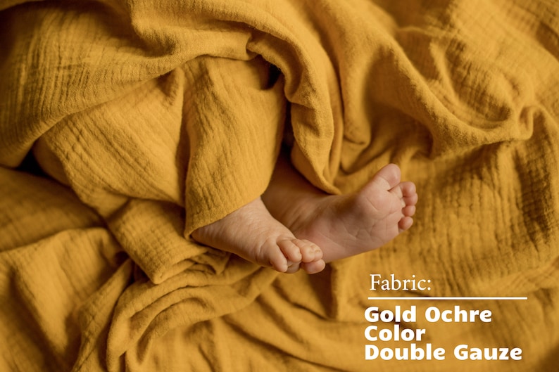 Pu&ograve; includere: I piedi di un bambino sono avvolti in un morbido tessuto di garza doppia giallo. Il tessuto &egrave; descritto come "Doppia garza color ocra dorata".