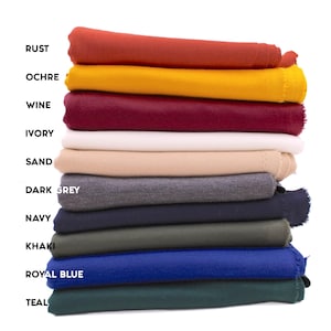 Könnte beinhalten: Ein Stapel von zehn Stoffproben in verschiedenen Farben, darunter Rost, Ocker, Wein, Elfenbein, Sand, Dunkelgrau, Marine, Khaki, Königsblau und Teal.