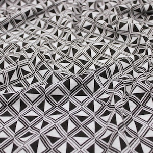 May include: Close-up of a black and white fabric with a geometric pattern. The design features repeating shapes of triangles and diamonds, creating a textured appearance. The fabric is draped, showing folds and shadows.