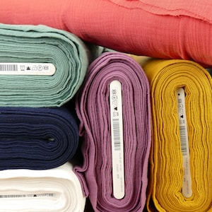 Pu&ograve; includere: Rotoli di tessuto in vari colori, tra cui verde acqua, blu navy, bianco, viola, giallo e azzurro. Ogni rotolo ha un'etichetta bianca con testo nero e un codice a barre.