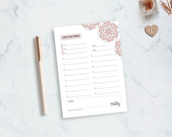 Könnte beinhalten: Ein weißer Notizblock mit einem roségoldenen Stift auf einer Marmoroberfläche. Der Notizblock hat ein To-Do-Listen-Layout mit dem Text "LET'S DO THIS!" und dekorativen roségoldenen Blumendesigns. Ein kleines goldenes Herz und Bürobedarf sind im Hintergrund.