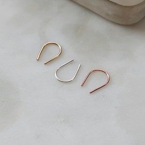 May include: Three small hoop earrings in different metal finishes: gold, silver, and rose gold. The hoops are simple and delicate, with a slightly curved shape.