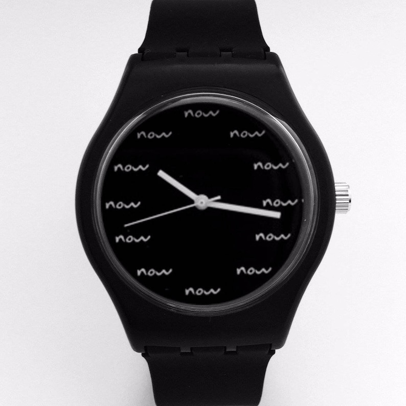 May include: A black wristwatch with a black silicone band and a black face. The face has white hands and the word "now" written around the edge of the face.