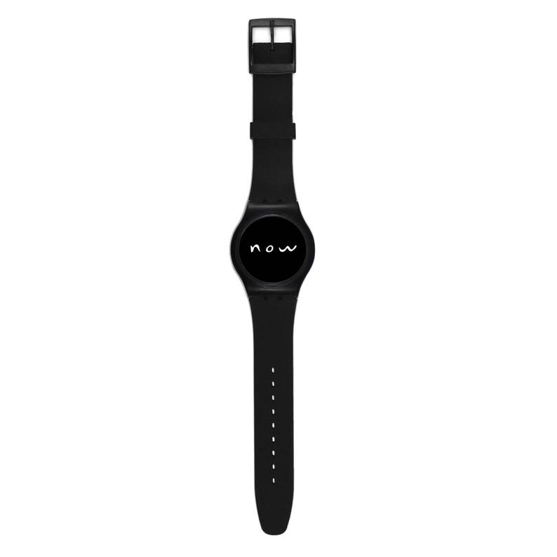 Puede incluir: Un reloj de pulsera negro con una correa negra y una esfera negra. La esfera del reloj tiene la palabra "now" escrita en blanco.