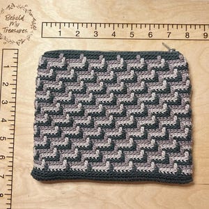 May include: A black and brown crocheted zippered pouch with a geometric pattern. The pouch is approximately 8 inches wide and 5 inches tall.