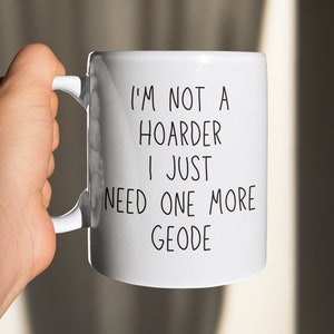 May include: White ceramic mug with a black inscription that reads "I'm not a hoarder I just need one more geode".