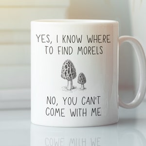 May include: White ceramic mug with a black and white illustration of morel mushrooms. The mug has the text "YES, I KNOW WHERE TO FIND MORELS NO, YOU CAN'T COME WITH ME" printed on it.