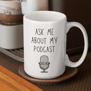 May include: White ceramic mug with a black outline of a microphone and the text "Ask me about my podcast" and "On Air" on the microphone.