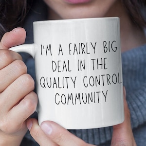 以下が含まれることがあります： 白いセラミック製のマグカップに、黒い文字で「品質管理コミュニティでは、私はかなり大きな存在です」と書かれています。