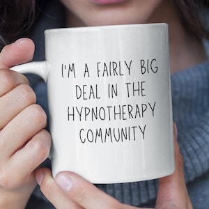May include: White ceramic coffee mug with black text that reads "I'm a fairly big deal in the hypnotherapy community".