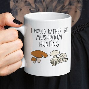 May include: White ceramic mug with a black handle. The mug has a brown and white mushroom illustration and the text "I would rather be mushroom hunting".