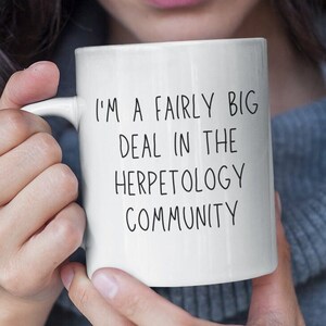 Peut inclure: Une tasse en céramique blanche avec du texte noir qui dit "Je suis un gros poisson dans la communauté de l'herpétologie".
