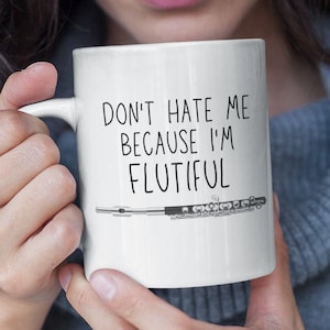 Peut inclure: Une tasse en céramique blanche avec une illustration en noir et blanc d'une flûte et le texte "Ne me déteste pas parce que je suis flutiful".