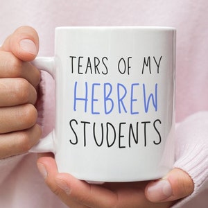 Pode incluir: Caneca de café de cerâmica branca com texto preto que diz "Tears of my Hebrew Students". O texto "Hebrew" está em azul.