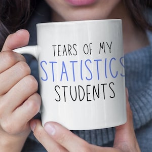 Könnte beinhalten: Eine weiße Keramiktasse mit dem Text "Tears of my Statistics Students" in schwarzer und blauer Schrift.