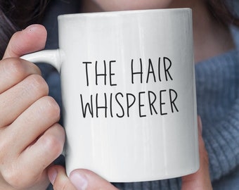 Puede incluir: Taza de cerámica blanca con texto negro que dice "The Hair Whisperer".