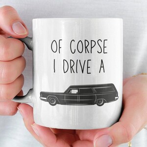 Puede incluir: Taza de cerámica blanca con una ilustración en blanco y negro de una carroza fúnebre y el texto "Of Corpse I Drive A".