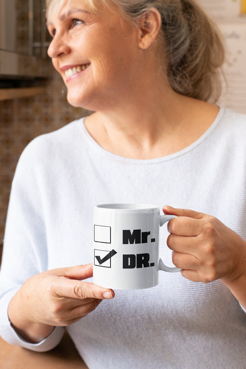 Op de afbeelding: Witte keramische mok met een zwarte checklist met de tekst "Mr." en "DR." met een vinkje naast "DR."