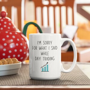 May include: White ceramic coffee mug with black text that reads "I'm sorry for what I said while day trading" with a blue upward trending graph.