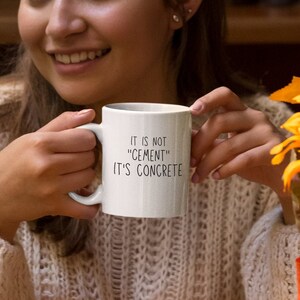 May include: White ceramic mug with black text that reads "It is not "cement" It's concrete".