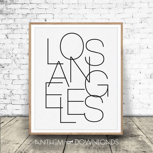 May include: Black and white graphic print of the word "Los Angeles" in a modern, geometric style. The print is framed in a light wood frame.