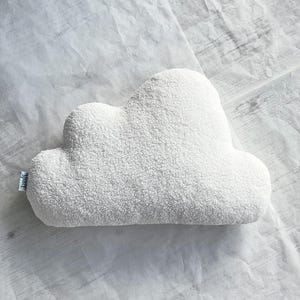 May include: A white cloud-shaped pillow with a textured, fluffy surface. The pillow is made of a soft material and has a tag on the side. The pillow is designed for decorative purposes.