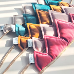 Puede incluir: Una colección de diademas de terciopelo de colores en tonos rosa, dorado, turquesa y beige. Cada diadema presenta un diseño triangular acolchado y una fina banda dorada. La etiqueta de cada diadema dice "SPACE".