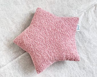Könnte beinhalten: Ein rosa sternförmiges Kissen mit einer strukturierten, plüschigen Oberfläche. Das Kissen hat ein Etikett mit der Aufschrift "Spact". Das Kissen ist ein weicher, dekorativer Artikel.