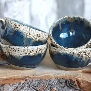 Peut inclure: Un ensemble de trois tasses en céramique présentant un émail bleu profond sur la moitié inférieure et un émail crème moucheté sur le bord supérieur. Chaque tasse possède un corps arrondi, une anse courbée et une finition intérieure lisse.