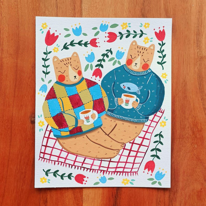 May include: A rectangular art print featuring two tan bears sitting on a red and white checkered blanket. One bear wears a multicolored checkered sweater, the other a teal sweater with a fish graphic. Both hold white mugs with tulip designs.