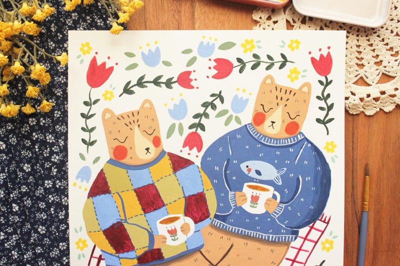 May include: A square art print featuring two bears sitting together. One bear wears a multicolored checkered sweater, the other a blue sweater with a fish graphic. Both hold white mugs with tulip designs, surrounded by red and blue floral motifs.