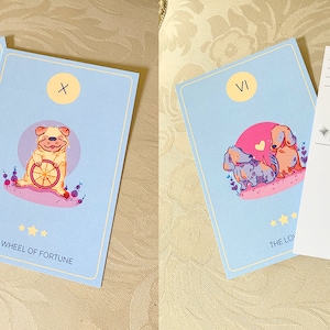 Puede incluir: Dos cartas de tarot ilustradas con un fondo azul claro. La carta de la izquierda es la carta de los Enamorados, que presenta a dos perros enamorados. La carta de la derecha es la carta de la Rueda de la Fortuna, que presenta a un perro sosteniendo una rueda con una rodaja de naranja.