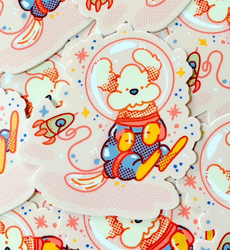 May include: A sticker featuring a cartoon dog wearing a space suit and helmet, floating in space with a rocket and stars. The sticker has a pink and white background with a dotted pattern.
