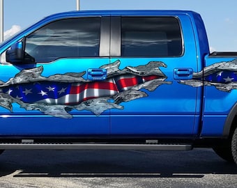 Könnte beinhalten: Ein blauer Pickup mit einem großen Aufkleber mit der amerikanischen Flagge an der Seite. Der Aufkleber ist so gestaltet, dass er aussieht, als wäre die Flagge zerrissen und zerrissen, wodurch die blaue Farbe des Pickups darunter sichtbar wird.