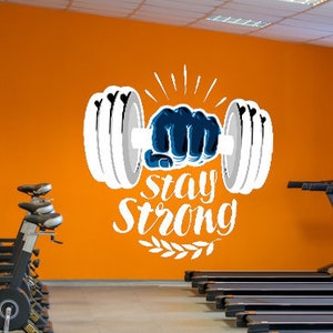 May include: A gym with a motivational quote on the wall that says "Stay Strong" with a graphic of a hand lifting a dumbbell. There are stationary bikes and treadmills in the gym.
