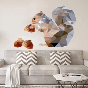 May include: A geometric wall decal of a squirrel holding an acorn, with a second acorn nearby. The squirrel is rendered in shades of gray, brown, and orange. The decal is placed above a gray sofa with chevron pillows.