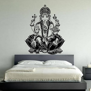May include: Black and white wall decal of Ganesha, the Hindu god of wisdom and prosperity, sitting in a lotus position. The decal is on a white wall above a black bed frame.