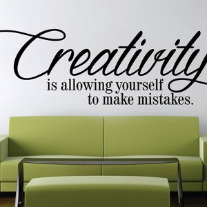 May include: A wall decal with the word "Creativity" in a cursive font, followed by the phrase "is allowing yourself to make mistakes." A green sofa and a glass-topped coffee table are in front of the wall.