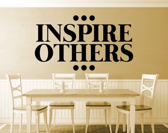 May include: A dining room scene featuring a wooden table and four white chairs. The wall above the table displays the words "INSPIRE OTHERS" in bold black letters. The room has a neutral color palette.