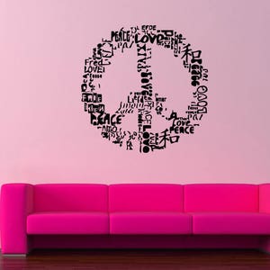 May include: A pink living room with a magenta sofa, a vase of flowers, and a wall decal. The wall decal is a peace symbol made of the words "peace" and "love" in multiple languages.