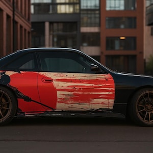 Könnte beinhalten: Schwarzes Sportwagen mit auffälliger rot-weißer Grafik. Das Auto hat bronzefarbene Leichtmetallfelgen und ein markantes Design an der Seite, möglicherweise inspiriert von japanischer Kunst. Das Auto steht auf einer Straße.