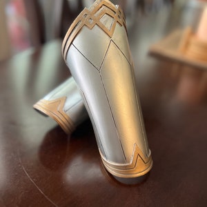 Puede incluir: Un par de brazaletes de plata y oro con un diseño geométrico. Los brazaletes están hechos de un material liso y brillante y tienen un diseño en relieve texturizado.