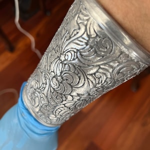 May include: A silver metal cuff bracelet with an intricate floral design.