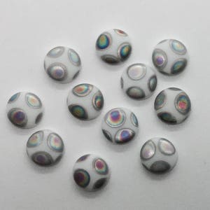 May include: Ten white iridescent round buttons with a pattern of smaller iridescent circles. The buttons have a slightly raised surface.