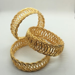 May include: Three gold bangles with a woven design. The bangles are stacked on top of each other.