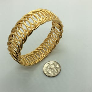 May include: A gold-toned bangle bracelet made of interlocking circles. The bracelet is about the size of a quarter.