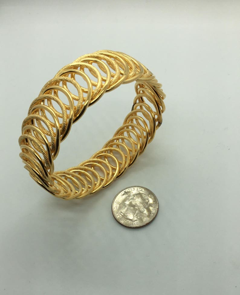 May include: A gold-toned bangle bracelet made of interlocking circles. The bracelet is about the size of a quarter.